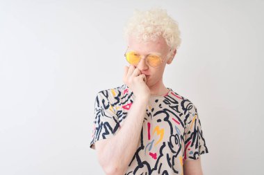 Renkli tişört ve güneş gözlüğü takan genç albino adam izole edilmiş kırmızı arka plan üzerinde gergin ve gergin görünüyor. Endişe sorunu.