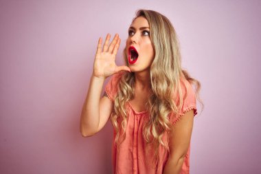 Pembe izole edilmiş arka planda duran tişört giyen genç ve güzel bir kadın el ele verip bağırıyor. İletişim konsepti.