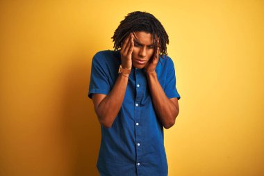 Rastgele kot gömlek giyen Afro bir adam izole edilmiş sarı arka planda duruyor. Başı ağrıyor çünkü stres altında. Migren ağrısı..