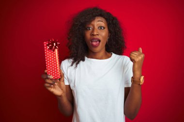 Sevgililer günü hediyesini elinde tutan Afrikalı genç bir Amerikalı kadın kırmızı arka planda durmuş gururla bağırıyor ve zaferi ve başarıyı kutluyor.