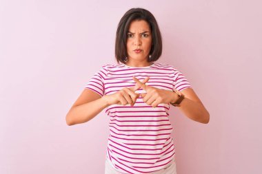 İzole edilmiş pembe arka plan üzerinde duran çizgili tişört giyen genç ve güzel bir kadın. Reddedilme ifadesinin negatif işaret vermesi için dua ediyorum.