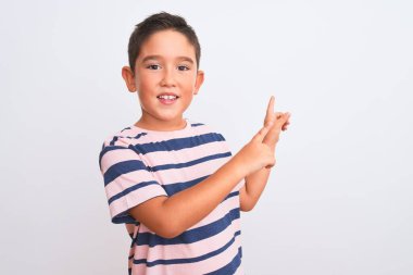 Güzel çocuk, günlük çizgili tişört giyip izole edilmiş beyaz arka planda duruyor gülümsüyor ve kameraya bakıyor. İki eliyle ve parmaklarıyla yan tarafa bakıyor..