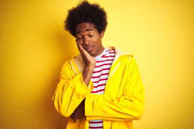 Siyah saçlı Afrikalı bir adam sarı arka planda dikilip kollarını kavuşturarak depresyondan sıkılmış ve yorgun gözüktüğünü düşünüyor..