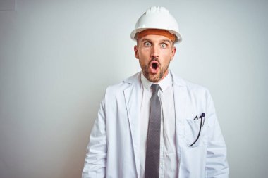 Güvenlik kaskı takan genç ve yakışıklı bir mühendis arka planda korku, korku ve heyecan dolu bir yüz ifadesiyle korkmuş ve şok olmuştu..