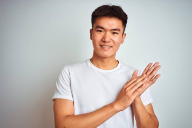 Asyalı genç bir Çinli tişört giyiyor. İzole edilmiş beyaz arka planda duruyor. Mutlu ve neşeli elleri alkışlıyor.