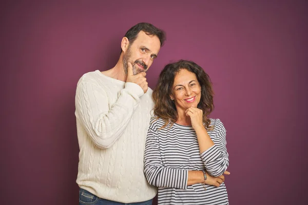 Beautiful middle age couple wearing winter sweater over isolated purple background looking confident at the camera smiling with crossed arms and hand raised on chin. Thinking positive.