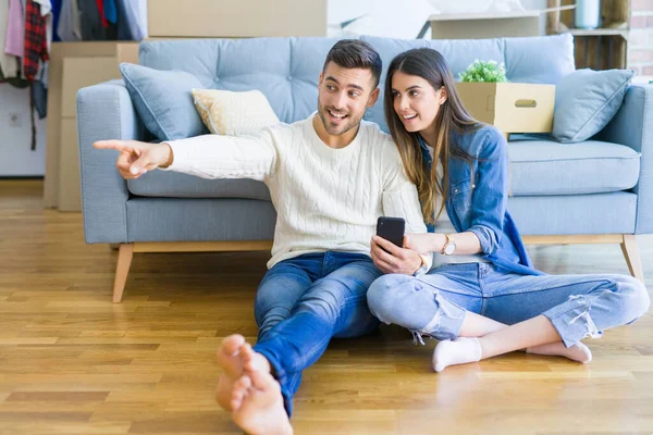 Νεαρό ζευγάρι κάθεται στο πάτωμα του νέου σπιτιού χρησιμοποιώντας smartphone ένα — Φωτογραφία Αρχείου