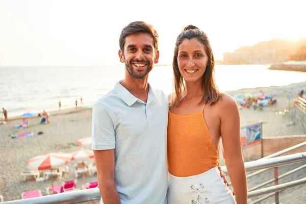 休暇中の若い美しいカップルの幸せと自信を笑顔 ビーチで抱きかかえて笑顔で立って — ストック写真