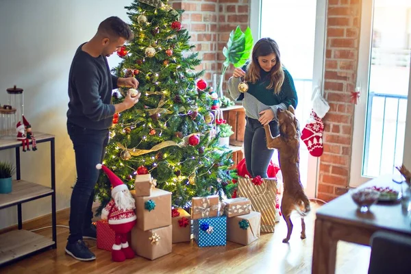 年轻漂亮的夫妇面带微笑 既快乐又自信 在家里站着装饰圣诞树 — 图库照片