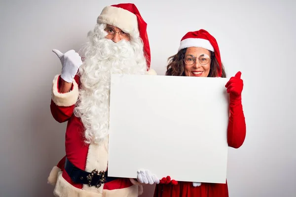 上了年纪的夫妇穿着圣诞老人的服装 拿着横幅在孤立的白色背景上 手握大拇指 笑容满面地站在一旁 — 图库照片