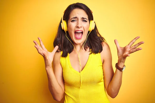 年轻的美女听音乐使用耳机在黄色孤立的背景庆祝疯狂和疯狂的成功与手臂抬起和闭上眼睛尖叫兴奋 优胜者概念 — 图库照片