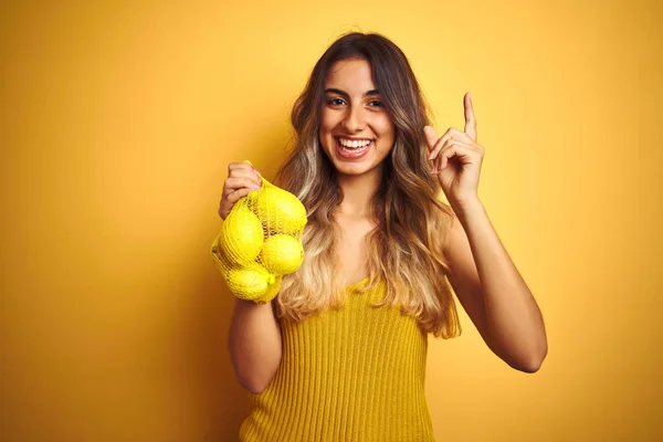 Mladá Krásná Žena Drží Síť Citronů Přes Žluté Izolované Pozadí — Stock fotografie