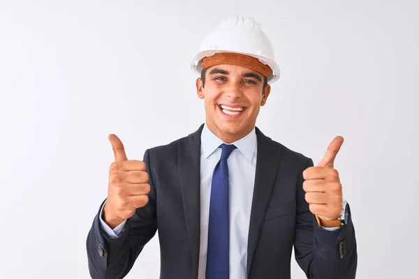 年轻英俊的建筑师 身穿西服 头戴头盔 站在孤立的白色背景上 手握积极的手势 微笑着竖起大拇指 喜形于色 快乐的表情和胜利的姿态 — 图库照片