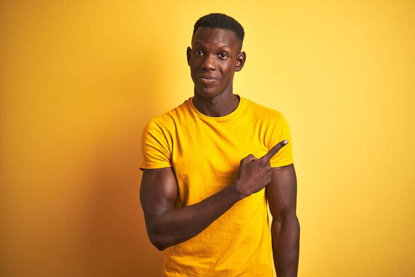 Young african american man wearing casual t-shirt standing over isolated yellow background Pointing with hand finger to the side showing advertisement, serious and calm face