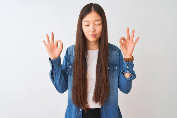 孤立した白い背景の上に立ってデニムシャツを着て若い中国の女性はリラックスし 指で瞑想のジェスチャーを行う目で笑顔を閉じます ヨガのコンセプト — ストック写真