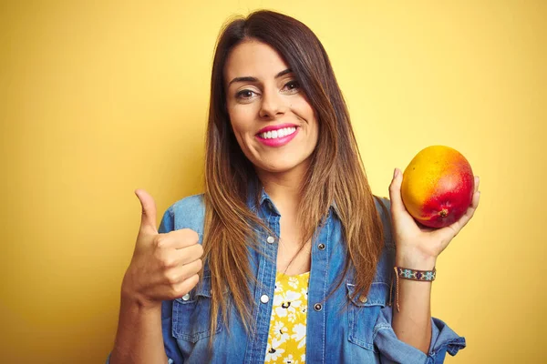 若いです美しい女性食べる新鮮な健康的なマンゴー上の黄色の背景幸せなで大きな笑顔を行いますOkサイン 指で親指アップ 優れたサイン — ストック写真