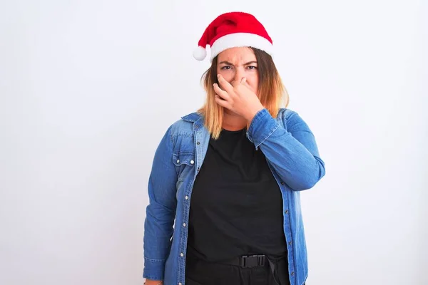 若い美しい女性は 孤立した白い背景の上に立ってクリスマスサンタの帽子を身に着けている何か臭いと嫌な 耐え難い匂いを嗅ぎ 鼻の上に指で息を保持する 悪い匂いの概念 — ストック写真