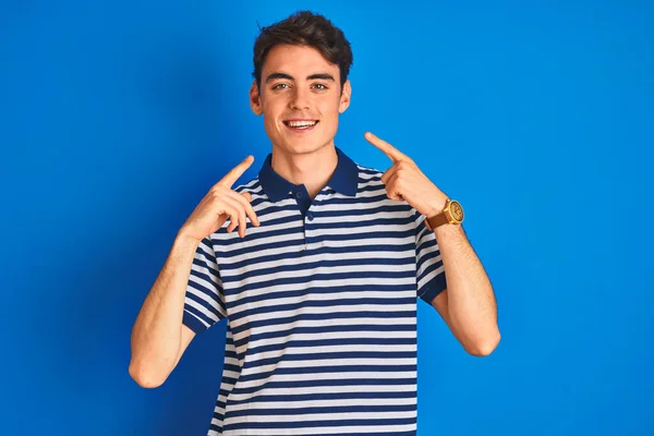 青の孤立した背景の上に立っているカジュアルなTシャツを着て10代の少年は 明るい表情と指の歯と口で指して笑っています 歯科衛生の概念 — ストック写真