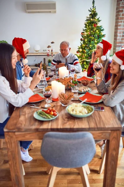 美丽的家庭戴着圣诞礼帽 面带微笑 快乐而自信 在家里用智能手机吃烤火鸡庆祝圣诞节 — 图库照片