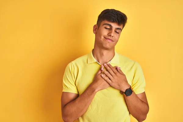孤立した黄色の背景の上に立つカジュアルなポロを身に着けている若いインド人男性は 目を閉じて胸に手で笑顔と顔に感謝のジェスチャー 健康コンセプト — ストック写真