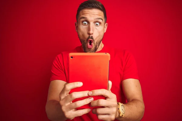 Joven Usando Tableta Digital Táctil Sobre Fondo Rojo Aislado Asustado — Foto de Stock
