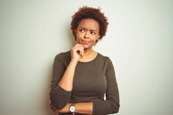 Young beautiful african american woman with afro hair over isolated background with hand on chin thinking about question, pensive expression. Smiling with thoughtful face. Doubt concept.