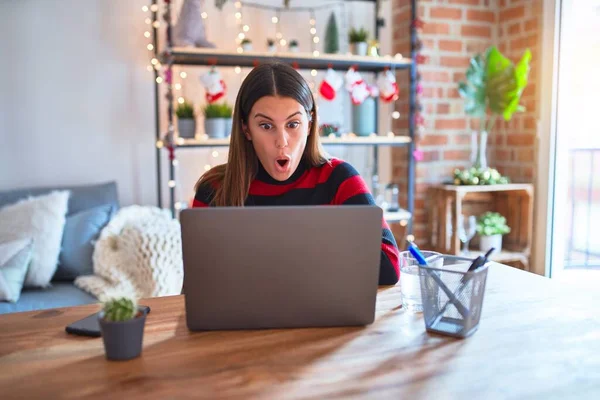 在圣诞节前夕 漂亮的女人坐在桌旁 带着笔记本电脑在家里工作 她的脸上充满了惊讶 恐惧和兴奋的表情 — 图库照片