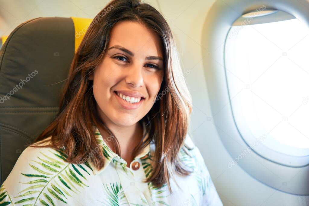 Young traveller woman sitting inside plane at the airport with sky view from the window