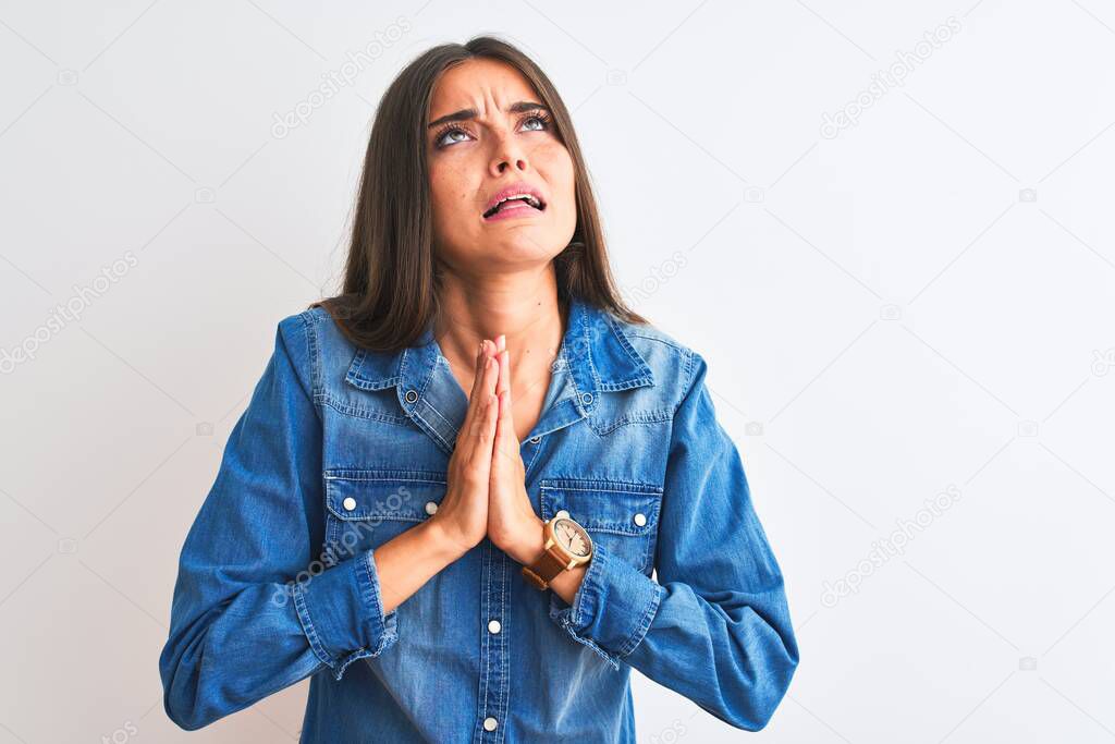Young beautiful woman wearing casual denim shirt standing over isolated white background begging and praying with hands together with hope expression on face very emotional and worried. Asking for forgiveness. Religion concept.