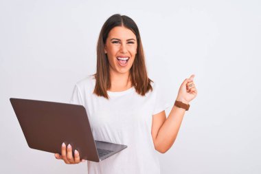 Güzel genç bir kadın bilgisayarını beyaz arka plan üzerinden kullanıyor. Neşeli bir yüzü var. Gülümsüyor ve mutlu ve doğal bir ifadeyle elini ve parmağını kaldırıyor.