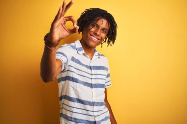 Sarı arka plan üzerinde çizgili tişört giyen Afro-Amerikan bir adam el ve parmaklarıyla tamam işareti yaparken gülümsüyor. Başarılı ifade.