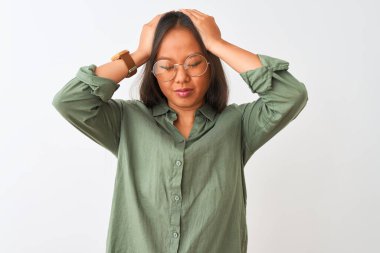 Yeşil gömlek ve gözlük takan Çinli genç bir kadın izole edilmiş beyaz arka planda acı ve migren yüzünden çaresiz ve stresli bir baş ağrısından muzdarip. Ellerini başının üstüne koy..
