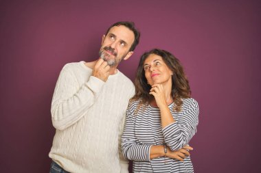 Güzel bir orta yaşlı çift, soyutlanmış mor arka plan üzerine kışlık süveter giyip elleri çenelerinde soru sorarken, düşünceli bir ifade takınıyorlar. Düşünceli bir yüzle gülümsüyor. Şüphe kavramı.