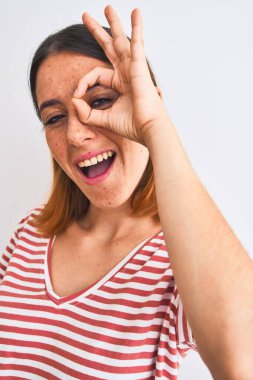 Güzel kızıl saçlı kadın izole edilmiş arka planda günlük kırmızı tişört giyiyordu. Gülümsüyordu. Tamam imzasını atarken parmaklarının arasından bakıyordu.