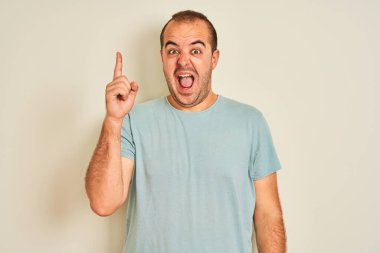 Mavi günlük tişört giyen genç adam izole edilmiş beyaz arka planda durup başarılı bir fikir işaret ediyor. Heyecanlı ve mutlu. Bir numara..