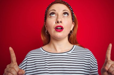 Güzel kızıl saçlı kadın çizgili donanma tişörtü giyiyordu. İzole edilmiş kırmızı arka plan üzerinde duruyordu. Şaşırmış ve şaşırmıştı..