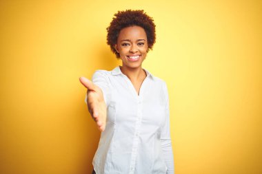 Afrika kökenli Amerikalı iş kadını izole edilmiş sarı arka planda dostça bir selamlama ve hoş geldin hediyesi olarak gülümsedi. Başarılı bir iş..