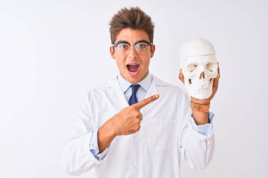 Gözlüklü yakışıklı doktor, izole edilmiş beyaz arka planda kafatasını tutuyor. Elle ve parmakla işaret ederek mutlu.