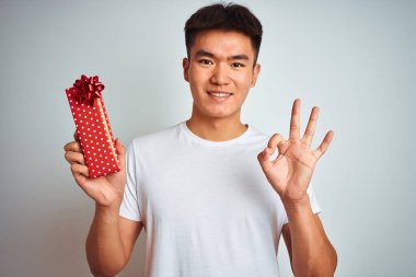 Sevgililer günü kartı tutan Asyalı genç adam izole edilmiş beyaz arka planda duruyor. Tamam işareti yapıyor, mükemmel bir sembol.