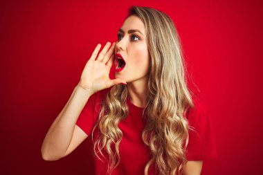 Genç ve güzel bir kadın, kırmızı izole edilmiş arka planda durup el ele tutuşarak bağırıyor ve çığlık atıyordu. İletişim konsepti.