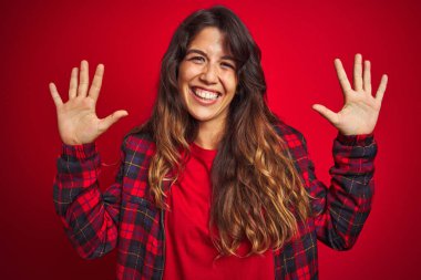 Kırmızı izole edilmiş arka plan üzerinde duran sıradan bir ceket giyen genç ve güzel bir kadın. Yüzünde kocaman bir gülümseme var. Parmağıyla kameraya bakıyor..