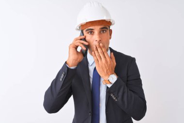 Miğfer takan genç mimar, akıllı telefonla konuşuyor. İzole edilmiş beyaz arka planda. Ağzı kapalı.
