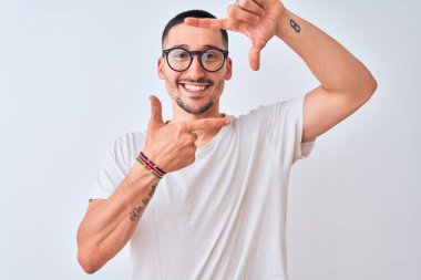 Gözlük takan ve izole edilmiş arka planda durup gülümseyen, elleri ve parmakları mutlu yüzlü genç bir adam. Yaratıcılık ve fotoğrafçılık kavramı.