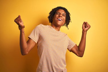 Sarı arka plan üzerinde duran çizgili tişörtlü Afro adam kolları havada ve gözleri kapalı bir şekilde başarıyı kutluyor ve şaşırıyor. Kazanan konsept.
