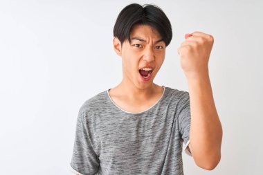 İzole edilmiş beyaz arka planda dikilen sıradan tişörtlü genç Çinli adam öfkeyle bağırıyor, deliriyor ve el kaldırarak bağırıyor.