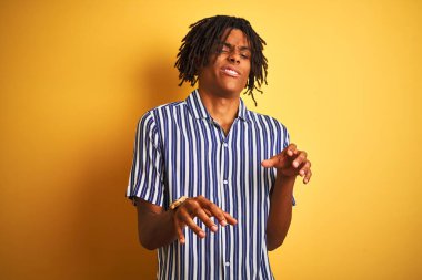 Rastgele çizgili tişört giyen Afro bir adam izole edilmiş sarı arka plan iğrenç yüz ifadesi, tiksindirici ve tiksindirici yüz ifadesi takınıyor çünkü iğrenme tepkisi veriyor. Eller havada. Can sıkıcı bir kavram..