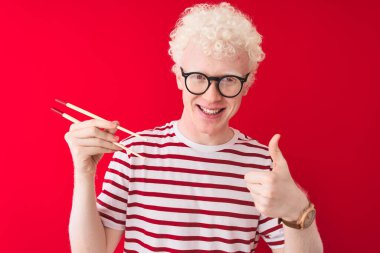 Genç albino sarışın adam yemek çubukları tutuyor. İzole edilmiş beyaz arka planda duruyor. Kocaman gülümsüyor.