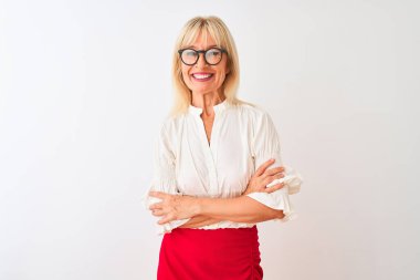 Tişört ve gözlük takan orta yaşlı iş kadını izole edilmiş beyaz arka planda durup kollarını kavuşturup kameraya bakarken gülümsüyor. Pozitif kişi.