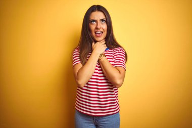 Çizgili tişört giyen genç ve güzel bir kadın izole edilmiş sarı arka planda durup bağırıyor ve boğuluyor çünkü acı verici bir boğulma. Sağlık problemi. Boğulma ve intihar konsepti.