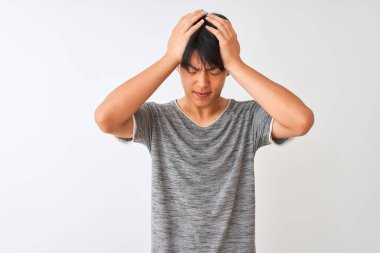 Genç Çinli bir adam, izole edilmiş beyaz arka planda dikilip acı ve migren yüzünden çaresiz ve stresli bir şekilde duran sıradan bir tişört giyiyor. Ellerini başının üstüne koy..